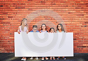 Well keep an eye on this space for you. Portrait of a group of young children holding a blank sign against a brick wall.