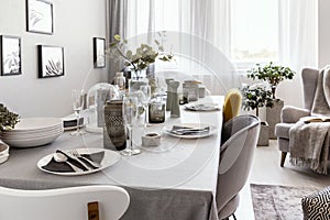 Well-laid table with plates and glasses in a grey dining room interior. Real photo