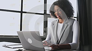 In a well-lit office, the businesswoman is captured typing on her laptop with a content smile