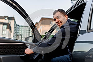 A well-looking man looks from his car and looks back. The driver is in a residential area of the city