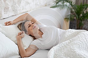 Well-rested blonde woman enjoying happy morning, stretching in bed, smiling