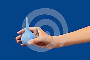 Wellgroomed womans hand holding enema on blue background