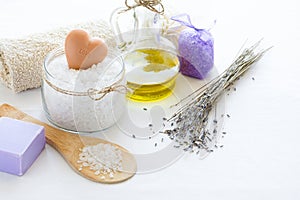 Wellness setting. Sea salt in glass, soap, towel, olive oil and flowers on white textured background