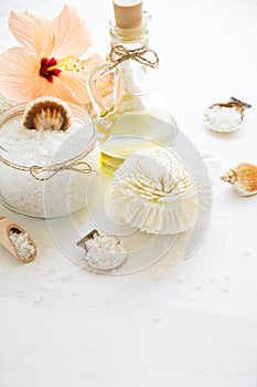 Wellness setting. Sea salt in glass, soap, towel, olive oil and flowers on white textured background