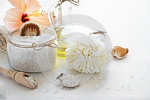 Wellness setting. Sea salt in glass, soap, towel, olive oil and flowers on white textured background.