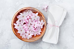 Wellness and spa composition of perfumed pink flowers water in wooden bowl and terry towel on gray stone table. Aromatherapy.