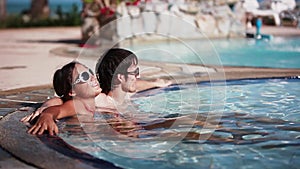 Wellness Spa couple relaxing in swimming pool outdoor at luxury resort spa retreat. Happy young woman and man in