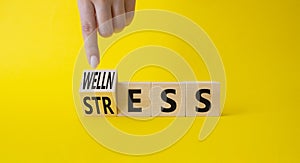 Wellness and Stress symbol. Busnessman hand. Turned Wooden cubes with word Wellness and Stress. Beautiful yellow background.