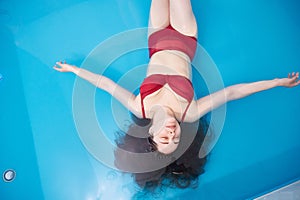 Wellness - young woman floating in Spa or swimming pool, she is very relaxed. Top view. Copy space.