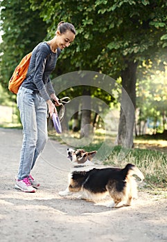 Welsh Corgi Pembroke dog and smiling happy woman walking together and playing outdoors, throwing her pet puller.