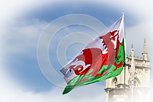 Welsh Dragon Flag flying in blue cloudy sky with the top of a castle like building in the background