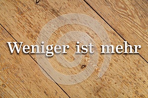 `Weniger ist mehr` text on a wooden background.  Translation: `Less is more`