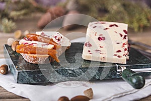 Wensleydale cheese with cranberries, red wine, honey, nuts, raisins on wooden cutting board. Black concrete background