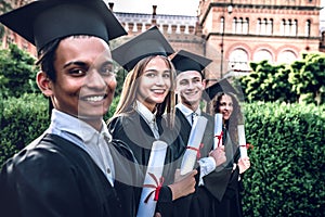 Were educated and ready to go!Happy graduates are standing in university outdoor in mantles with diplomas in hand smiling and