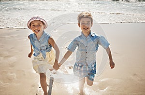 Were so excited to be at the beach. two adorable young children running hand-in-hand on the beach.