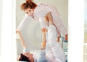 Were having a pajama night. a young mother lifting her daughter with her legs while lying on bed.