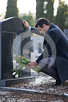 They were her favorite flowers. Shot of a young man visiting a gravesite with a bunch of flowers.