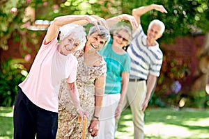 Were not young but we live like it. a group of smiling seniors exercising outside.