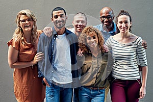 Were one happy team. Portrait of a group of people standing together against a wall outside.