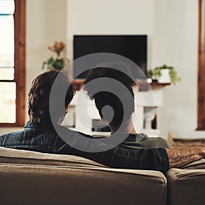 Were turning into couch potatoes today. Rearview shot of a young couple sitting on sofa and watching tv together at home