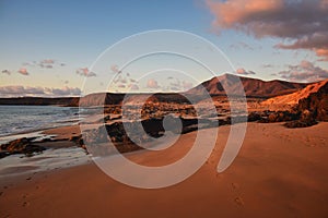 The west coast of Lanzarote at a beautiful sunset. A beach and a blue sky with some clouds. View to the mountain range Los Ajaches