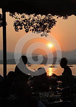 West Lake Xi Hu sunset in Hangzhou, Zhejiang Province, China with silhouettes of people.
