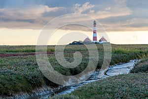 Westerhever lighthouse sand at sunset and clouds with canal in the foreground