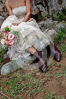 A western brides stylish brown boots holding an elegant flower bouquet. Sitting on a step in a vintage wedding dress