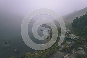 Mlhavé ráno pohled v mokré horské oblasti ve slovenských Tatrách. panorama horského jezera. turistická stezka - vzhled vintage filmu