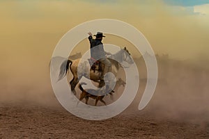 Western cowboy riding horses with dog in cloud of dust in the sunset