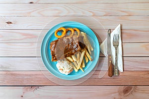 BBQ pork ribs, onion rings, french fries and coleslaw in blue plate on table