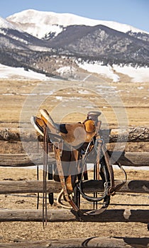 Western leather riding saddle with stirrups and pommel horn on rustic wood ranch fence photo