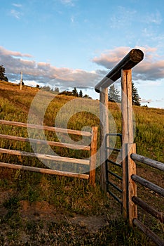 Western pasture scene with wood fence and log entryway with metal gate, evening light, Eastern Washington state, USA