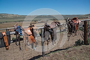 Western riding tack saddles, bridles and horse blankets on wooden corral post after a trail ride