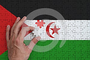 Western Sahara flag is depicted on a puzzle, which the man`s hand completes to fold