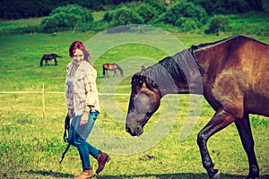 Western woman walking on green meadow with horse