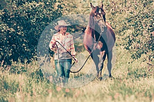 Western woman walking on green meadow with horse