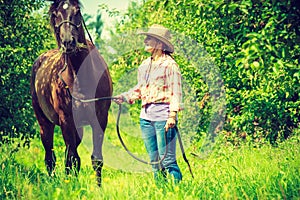 Western woman walking on green meadow with horse