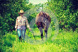 Western woman walking on green meadow with horse