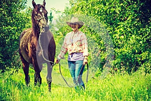 Western woman walking on green meadow with horse