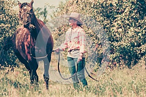 Western woman walking on green meadow with horse