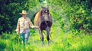 Western woman walking on green meadow with horse