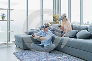 A western young couple wearing VR or virtual reality glasses, headsets sitting and playing a video game on sofa in front of TV at