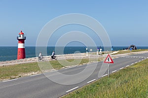 Lighthouse at dike with passing bikers near Westkapelle, the Netherlands