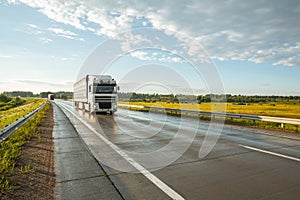 Wet asphalt road with a big truck against the blue sky