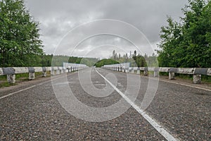 Wet asphalt road surrounded by forest . Cloudy sky. photo