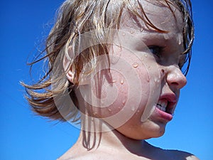Wet baby after swimming in the sea. Portrait of a girl. Wet hair and face. A grimace on the face of the child. Blue sky and yellow