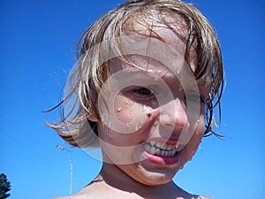 Wet baby after swimming in the sea. Portrait of a girl. Wet hair and face. A grimace on the face of the child. Blue sky and yellow