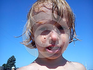 Wet baby after swimming in the sea. Portrait of a girl. Wet hair and face. A grimace on the face of the child. Blue sky and yellow