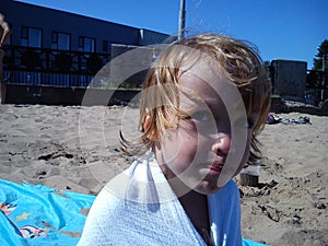 Wet baby after swimming in the sea. Portrait of a girl. Wet hair and face. A grimace on the face of the child. Blue sky and yellow